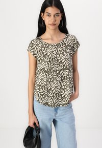 Krátky rukáv, olivovo zelený top s bielym paisley vzorom, z mäkkého materiálu, s okrúhlym výstrihom a voľným strihom. V kombinácii s svetlomodrými džínsami.