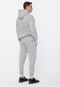 Szary komplet z bluzy i spodni dresowych, wykonany z miękkiego materiału, z dużym kapturem, ściągaczami na rękawach oraz bocznymi kieszeniami, uzupełniony czarnymi butami.