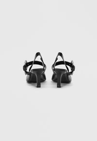 Μαύρα δερμάτινα σανδάλια με τακούνι και λουράκια στον αστράγαλο, διακοσμημένα με μεταλλικές λεπτομέρειες στα λουράκια και με λεπτό, ψηλό τακούνι.