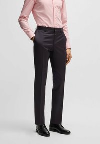 Op maat gemaakte donkere broeken van een gemengde stof met een gladde textuur, voorzien van zijzakken en een slim fit. Gedragen met een lichtroze overhemd met knopen.