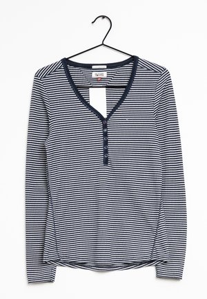 T-shirt Henley à manches longues rayé bleu marine et blanc avec cinq boutons et un col en V, suspendu sur un cintre noir.