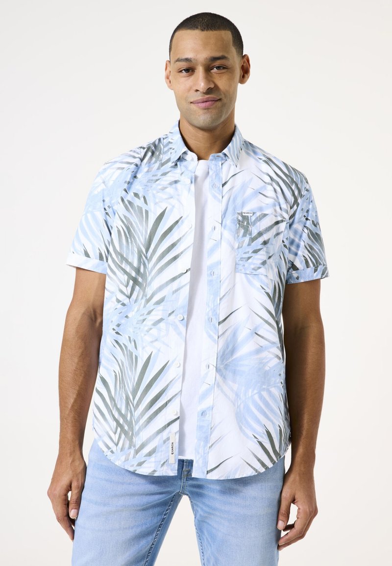 Camisa de botones de manga corta en blanco con patrones de hojas de palma en azul y verde, que incluye un bolsillo en el pecho y un dobladillo curvado.