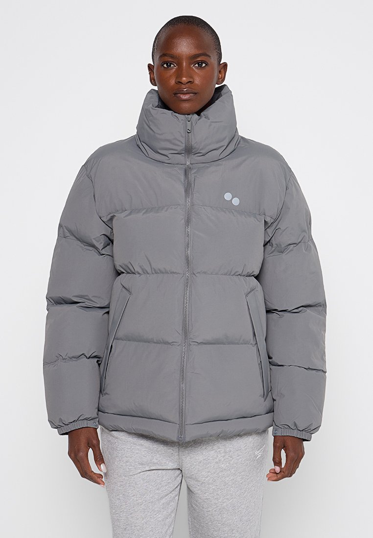 Graue Pufferjacke mit hohem Kragen, Reißverschluss und horizontaler Steppung. Verfügt über zwei seitliche Taschen und ein dezentes Logo auf der Brust.