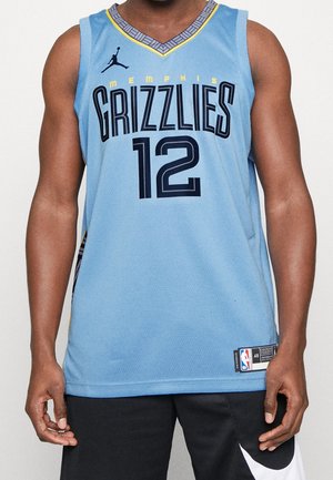 Mężczyzna ubrany w jasnoniebieską koszulkę do koszykówki Memphis Grizzlies z numerem 12 oraz czarne spodenki z białym logo Nike, stoi na białym tle.