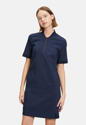 Robe bleu marine à manches courtes avec un col zippé et une coupe droite, présentant une texture lisse et un minimum de détails.
