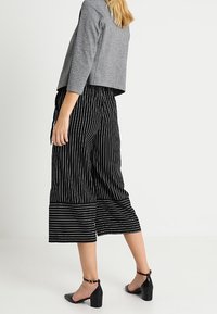Culotte a righe bianche e nere con design a gamba larga, abbinati a un maglione cropped grigio e sandali neri con tacco. Texture liscia.