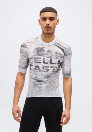 Joven vistiendo un maillot de ciclismo ajustado de manga corta con patrones abstractos en blanco y negro y pantalones cortos de ciclismo negros.