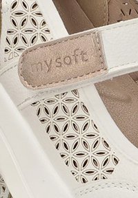Sandalia blanca con patrón floral recortado, que presenta una correa beige etiquetada como "mi suave". Hecha de material sintético con una textura suave.