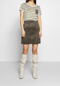 Gestreiftes grün-beiges T-Shirt mit einer Tasche, kombiniert mit einem braunen Wildleder-Minirock mit einem Reißverschluss vorne und kniehohen beigen Stiefeln.