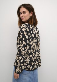 Black floral blouse featuring beige abstract flower patterns, long sleeves, a round neckline, and a loose fit. Soft, lightweight fabric.