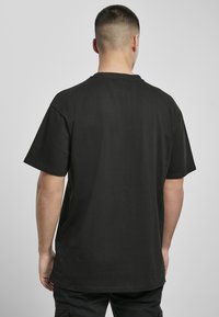 Mustmust toonkiga lühikeste varrukatega T-särk mustast puuvillast, vaadatuna selja tagant. Kanga pind näeb välja sile, lõige on mugav ja disain on minimalistik.