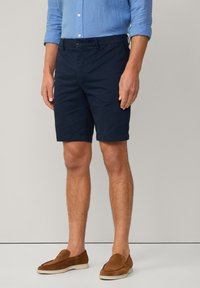 Shorts bleu marine dans un design ajusté, en coton, dotés de poches avant et d'une finition soignée à l'ourlet, associés à des chaussures à enfiler marron.