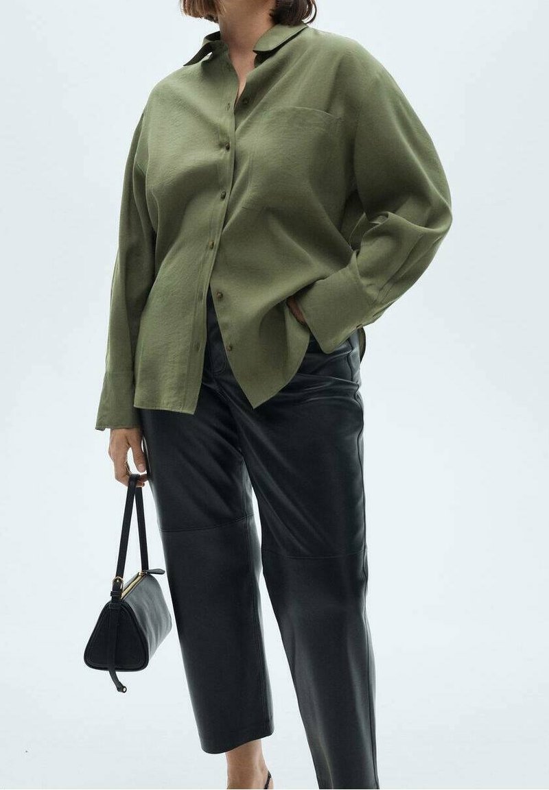 Chemise ample boutonnée vert olive avec une poche, associée à un pantalon en cuir noir taille haute. Sac à main noir en main.