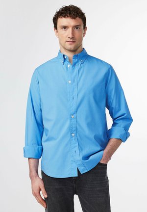 Ljusblå button-up skjorta med spridd krage, lång ärm som är uppkavlad vid manschetterna, och ett mjukt, strukturerat tyg.