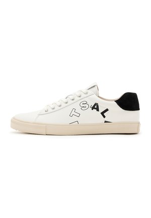 Sneaker en cuir blanc avec des accents noirs au talon, présentant de grandes lettres noires sur le côté et une semelle en caoutchouc. Design minimaliste.