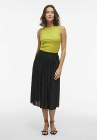Un débardeur vert côtelé associé à une jupe midi plissée noire. La tenue présente une silhouette ajustée et des sandales plates noires.