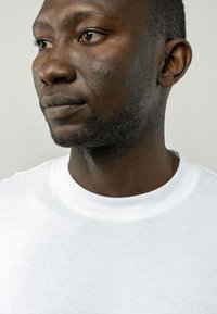 Witte katoenen crewneck t-shirt gedragen door een persoon met een donkere huid. De stof lijkt zacht met een gladde textuur en minimale naden.