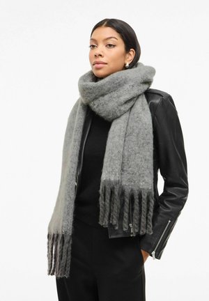 Grå ullskjerf med myk tekstur, med frynsete kanter og en koselig fall, kontrastert mot et svart antrekk og skinnjakke.