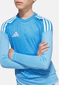 Maglietta atletica a maniche lunghe azzurro chiaro con motivi testurizzati e strisce bianche sulle spalle. Presenta un logo Adidas sulla parte anteriore.