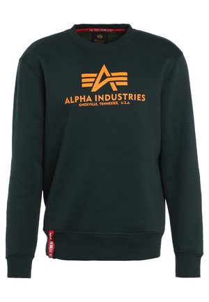 Sweatshirt vert foncé en matière douce, avec un logo "ALPHA INDUSTRIES" orange et des bandes d'accent sur le devant. Poignets et ourlet côtelés.