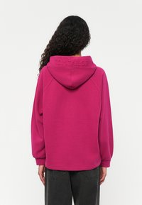 Fuchsia Kapuzenpullover mit weicher Textur, abgerundeten Schultern und geprägtem "TOM TAILOR"-Logo am Kragen.