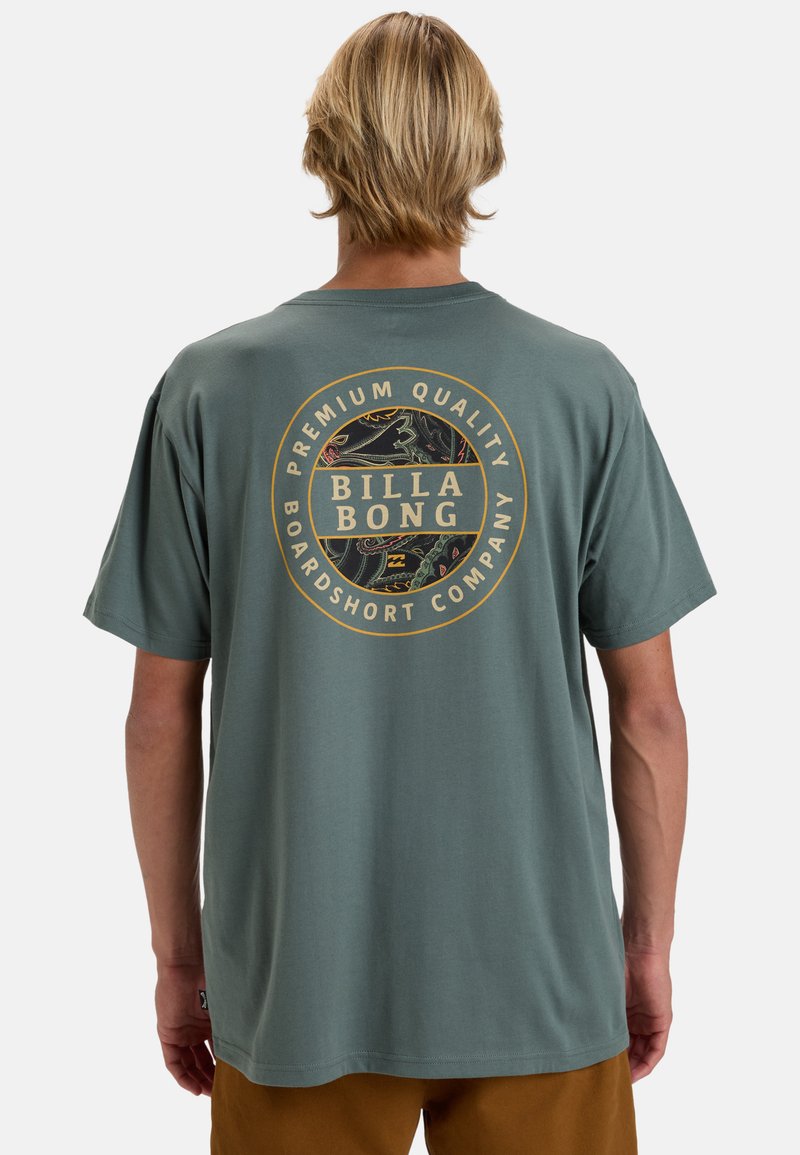 Grünes Baumwoll-T-Shirt mit einem kreisförmigen Logo in Gold und Schwarz auf dem Rücken, kurzem Ärmel und lässiger Passform.