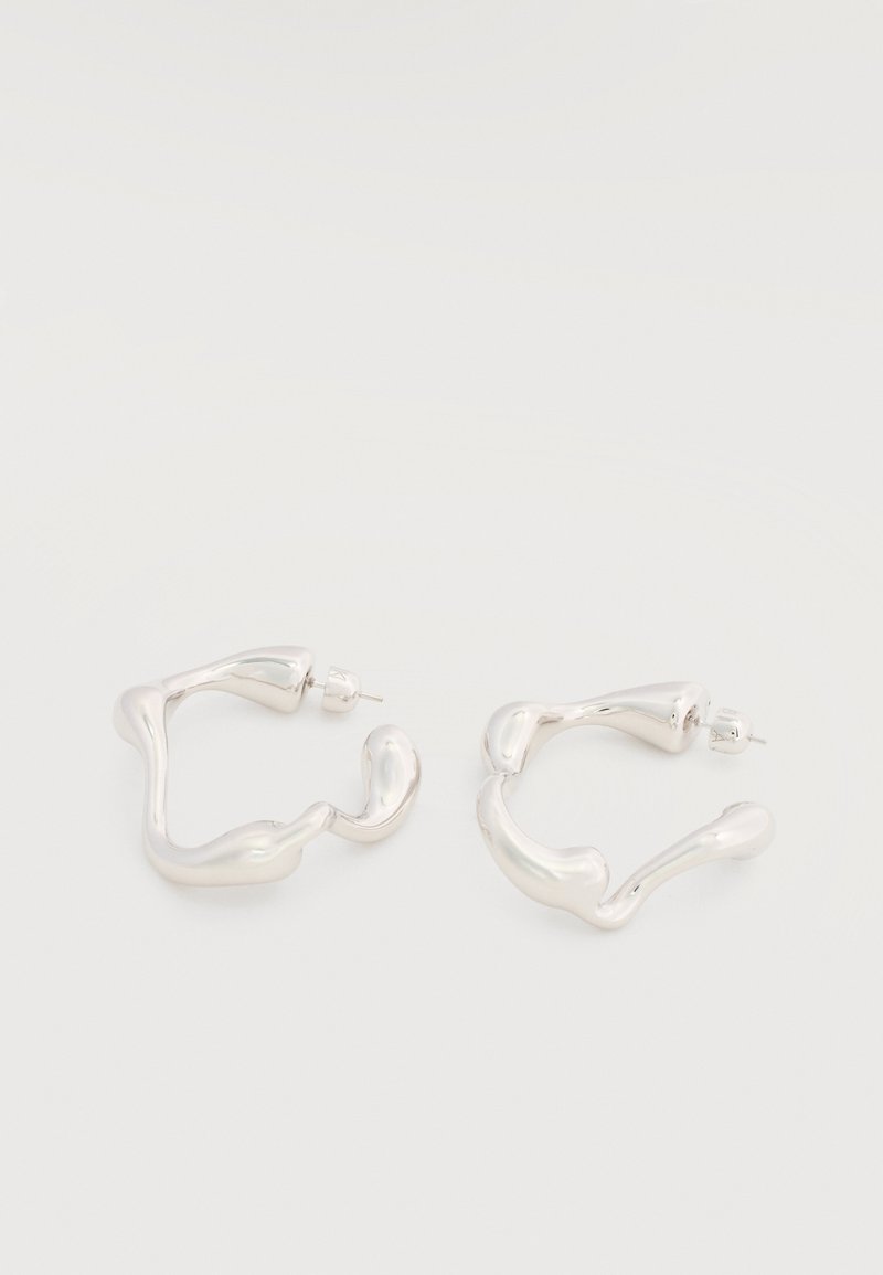 Ζευγάρι από ακανόνιστα σχήματα ασημένια σκουλαρίκια κρίκους με καρφωτά πίσω μέρη σε λευκό φόντο.