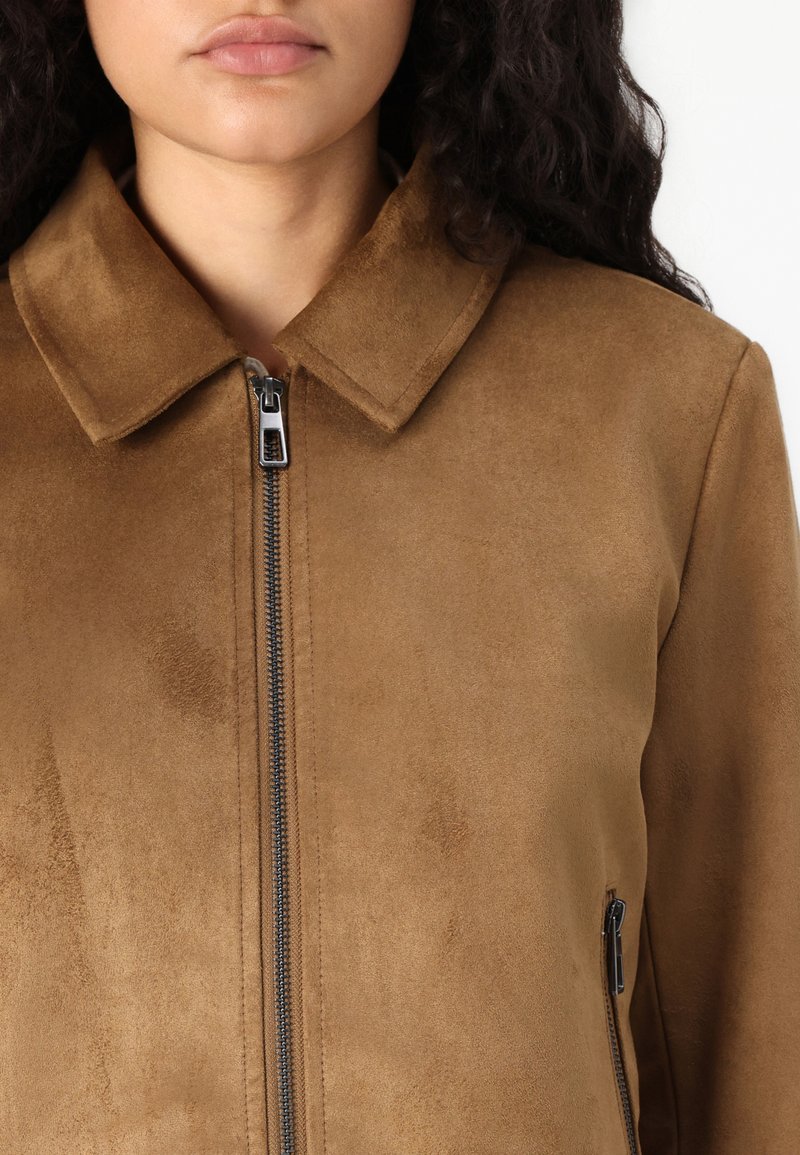 Giacca in finta suede marrone con colletto, zip frontale e tasche laterali. Texture liscia e design minimalista.