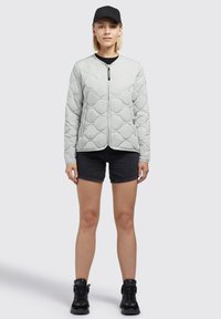Lichtgrijze gewatteerde jas met een ronde halslijn, ritssluiting, geribbelde manchetten en een gladde textuur, gedragen over een zwart shirt en shorts.