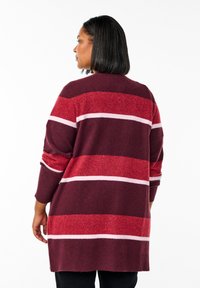 Lång stickad cardigan i vinröd, röd och rosa ränder. Har en avslappnad passform, ribbade ärmslut och rund halsringning. Mjuk textur.