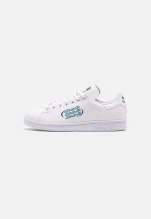 Białe buty sportowe Adidas Stan Smith z niebieskim logo po boku i na pięcie, z białymi sznurowadłami i płaską podeszwą na jednolitym tle.