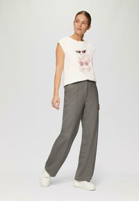 Biała bezrękawnikowa koszulka z ilustracją kolorowych okularów przeciwsłonecznych, w połączeniu z szarymi spodniami o wysokim stanie i białymi trampkami. Prosty design i luźny krój.