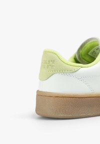 Baskets en cuir blanc avec des accents en suède vert et une semelle en caoutchouc brun texturé. Comprend des coordonnées embossées sur le talon.