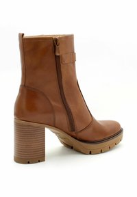 Stivaletto in pelle marrone con zip laterale, tacco rettangolare, suola a pianta testurizzata e un'accortezza a cinturino vicino alla caviglia.