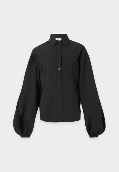 Μαύρο πουκάμισο με μακριά μανίκια και κουμπιά, με μυτερό γιακά και φουσκωτά μανίκια μαζεμένα στις μανσέτες, σε μονόχρωμο ανοιχτό φόντο.