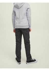 Felpa grigia con cappuccio e polsini a costine, abbinata a jeans scuri e sneakers nere con suole bianche, vista da dietro.