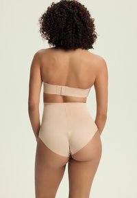 Beżowy bezszwowy biustonosz strapless oraz wysokie majtki w gładkim materiale. Biustonosz ma zapięcie na haczyk i oczko; majtki mają krótki krój.