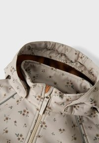 Beige blomsterjakke med hætte, der har små blomstermønstre, en brun foring og en frontal lynlås. Glat stof med elastiske kanter.