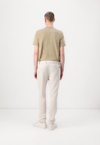 Beige Kurzarmhemd mit geradem Schnitt, kombiniert mit hellgrauen, schmal zulaufenden Hosen und weißen Sneakers. Minimalistisches Design, glatte Texturen.