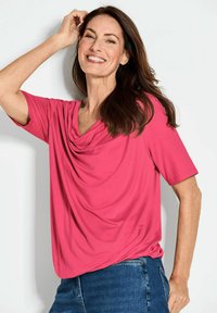 Rosa, drapierter Oberteil aus einem weichen, leichten Stoff, mit einem Schalkragen und kurzen Ärmeln, kombiniert mit Jeans.