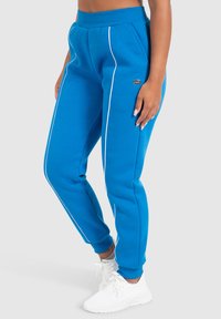 Blaue Sweatpants aus weichem Stoff, mit weißen Seitenstreifen und gerippten Bündchen. Beinhaltet ein kleines Markenlogo auf der Hüfte.