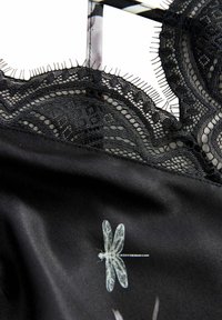 Țesătura de satin negru are dantelă neagră intricate la guler și un imprimeu cu libelule albe. Marginile dantelei texturate creează un contrast vizual.