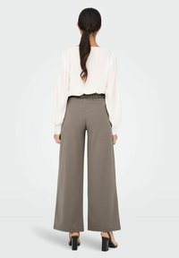 Vide ben, grå bukser med elastisk liv, kombinert med en langermet, hvit bluse. Har et minimalistisk design og glatt tekstur.