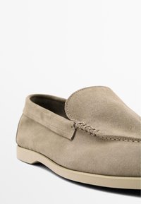 Mocassini in suede beige chiaro con suola piatta in gomma, dotati di punta arrotondata, dettagli cuciti e design con tomaia a pieghe.