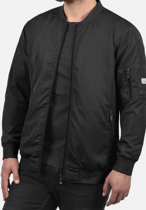 Black bomber jacket with a zip front, ribbed cuffs and hem, side pockets, and a utility pocket on the sleeve. Smooth, lightweight material.