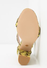 Żółto-czarna sandał na wysokim obcasie z teksturowaną cholewką i gładką beżową podeszwą, z wycięciem na palce i paskiem wokół kostki.