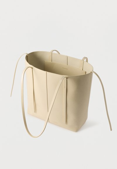 Μπεζ δερμάτινη τσάντα tote με δύο μακριές λαβές, ανοιχτό πάνω μέρος και ελάχιστες ραφές, σε απλό λευκό φόντο.