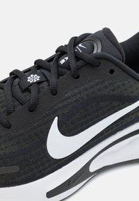 Scarpa atletica nera Nike con tomaia in tessuto testurizzato, logo Swoosh bianco, lacci piatti e suola imbottita con outsole nera.