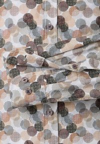 Gemusterte Hemd mit Knöpfen aus leichtem Stoff, das große Kreise in erdigen Tönen von Braun, Beige und Grün zeigt, kombiniert mit kontrastierenden gepunkteten Texturen.