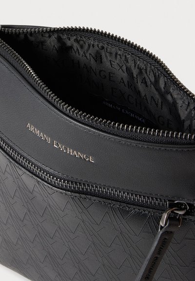 Близък план на отворена черна чанта Armani Exchange с десен отвън, цип, подплата с марка и метални елементи.